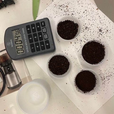 ground coffee in cups shown with a calculator and instruction manual for coffee grinder testing